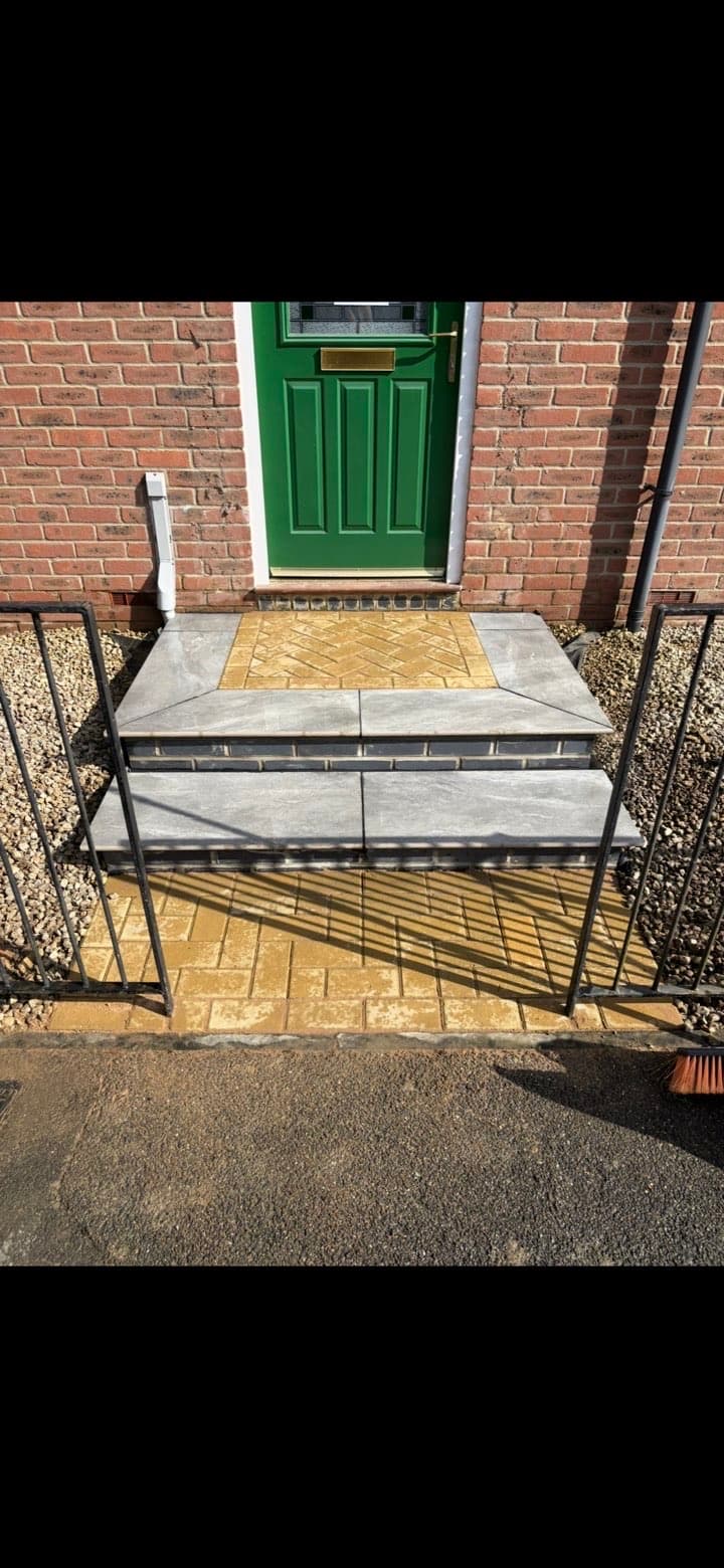 Two-tier grey stone steps with yellow herringbone brick inlay leading to a green front door.