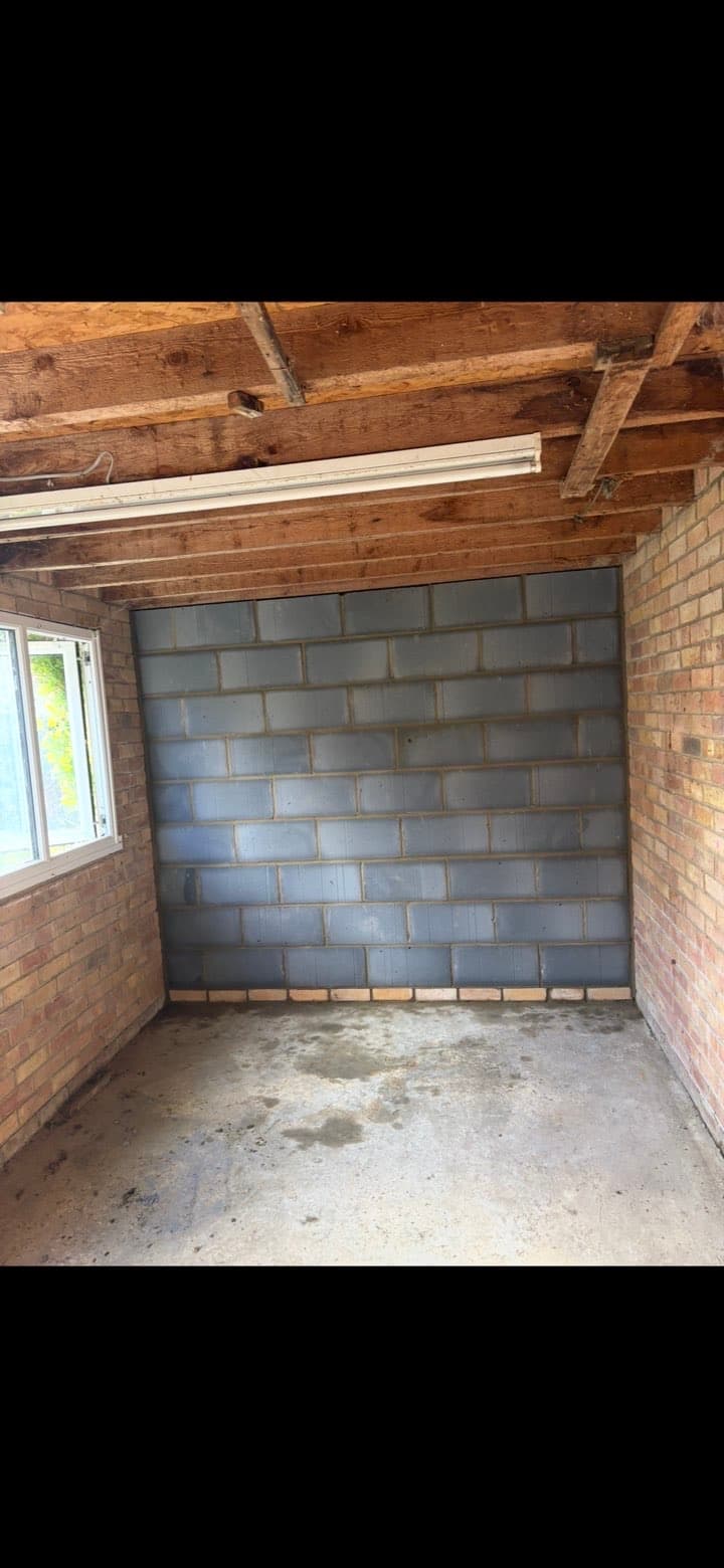 Grey cinder block wall built inside a brick garage with exposed wooden ceiling beams.