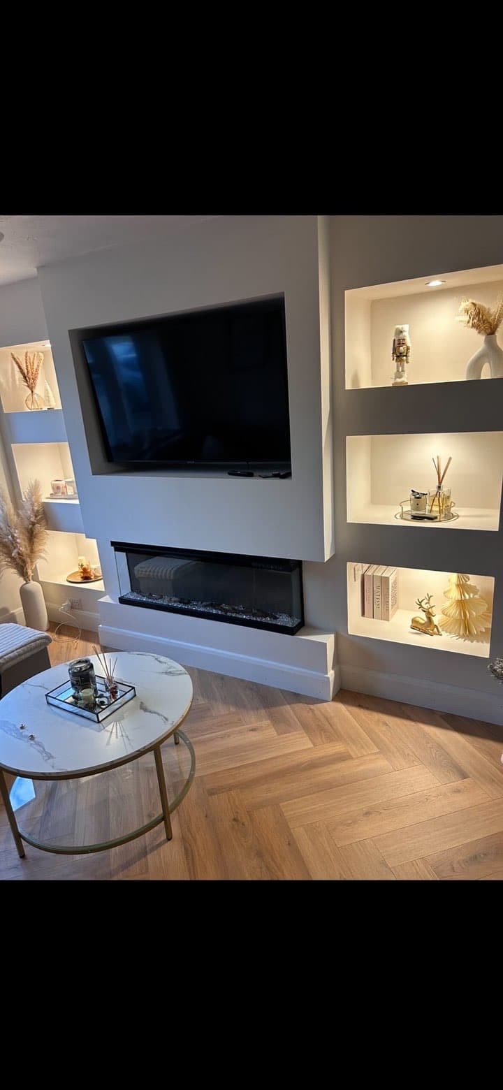 Modern living room featuring built-in TV, electric fireplace, illuminated wall niches, and herringbone flooring.