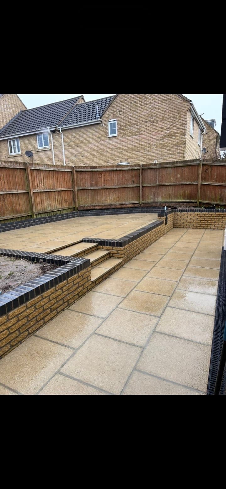 Tiered stone patio with brick retaining walls and wooden fencing in a residential backyard.