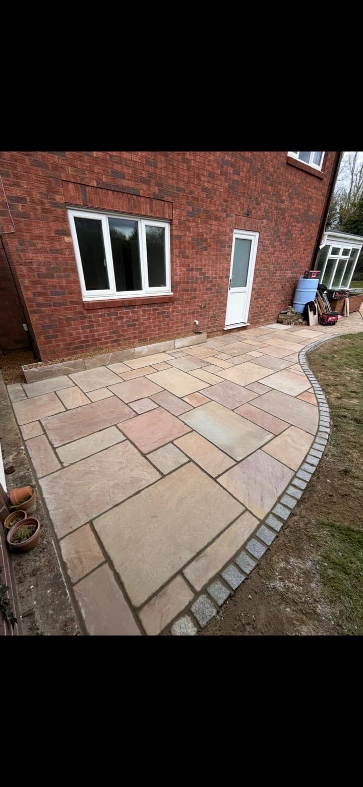 Multi-colored sandstone patio with a curved cobblestone border outside a red brick house.